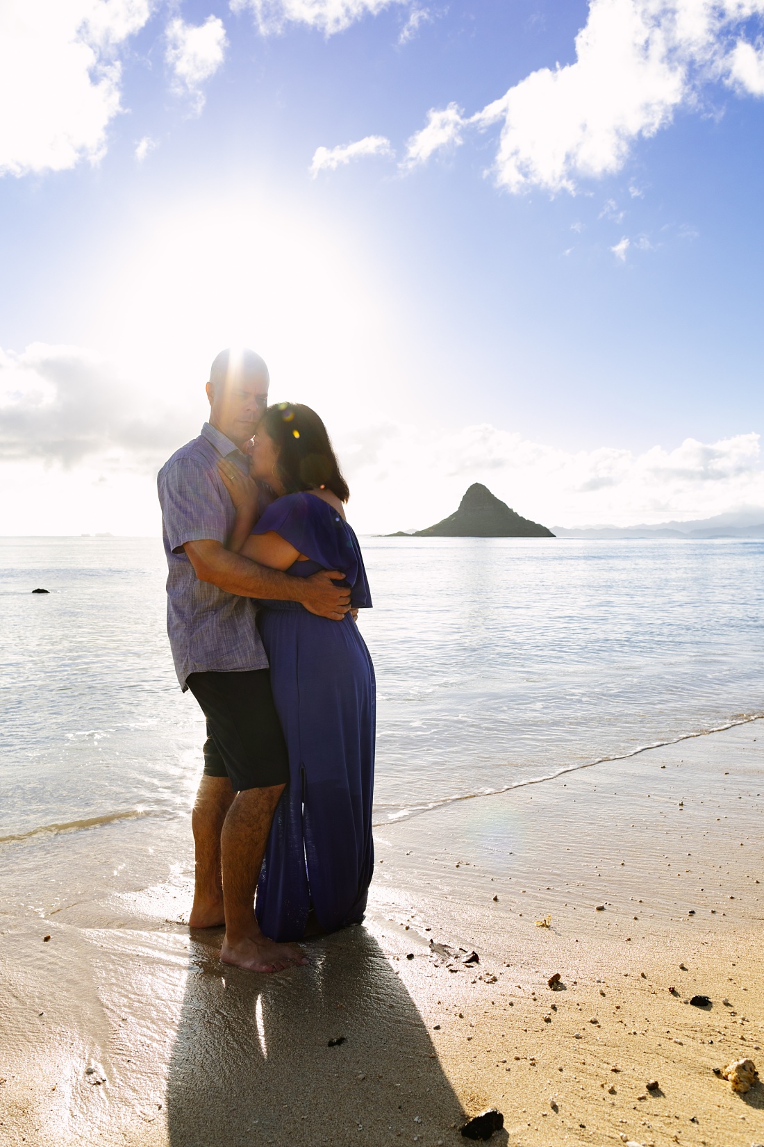 a couple snuggles at sunrise with chinaman's hat behind
