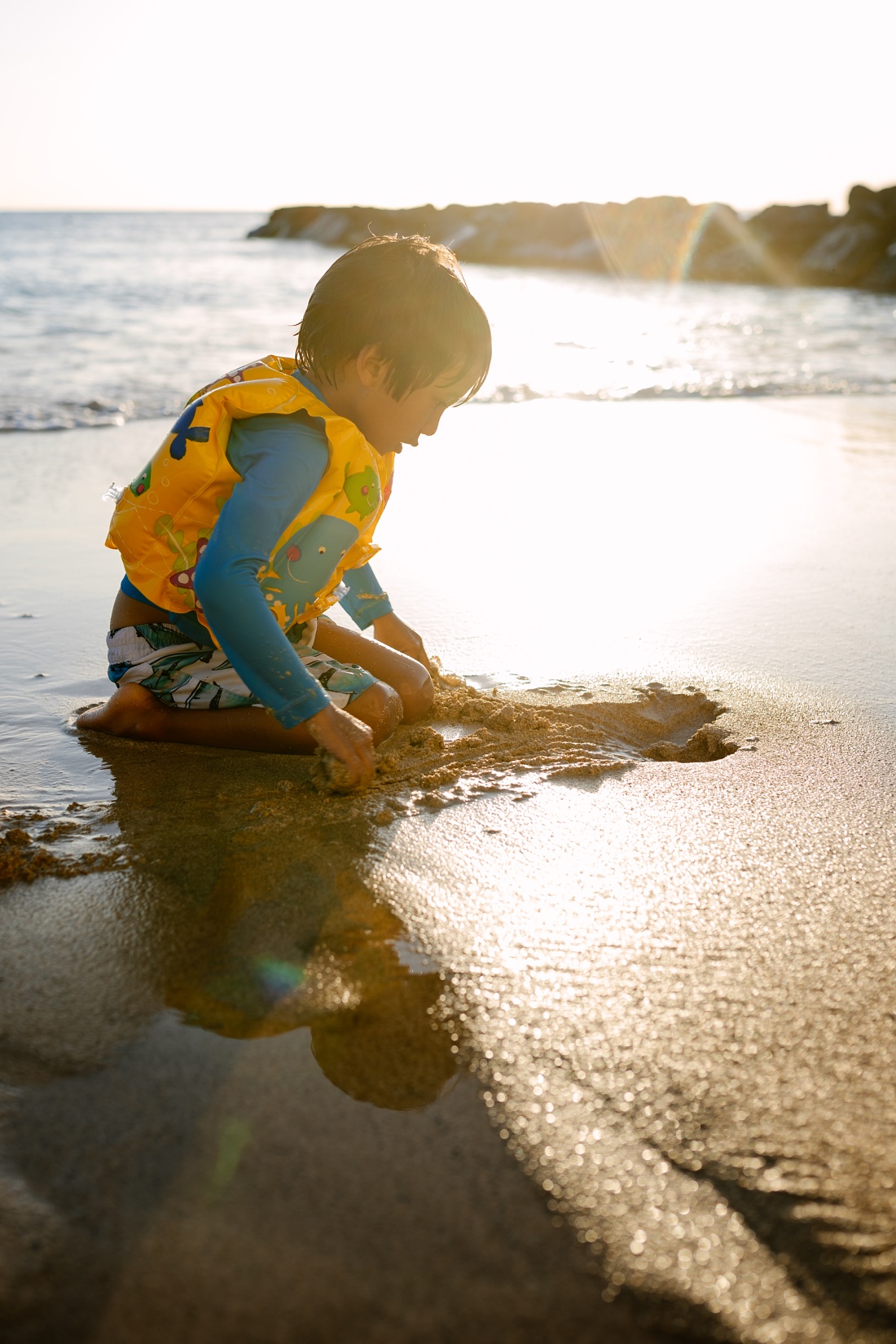 boy playing in the sand in waikiki with sun flare