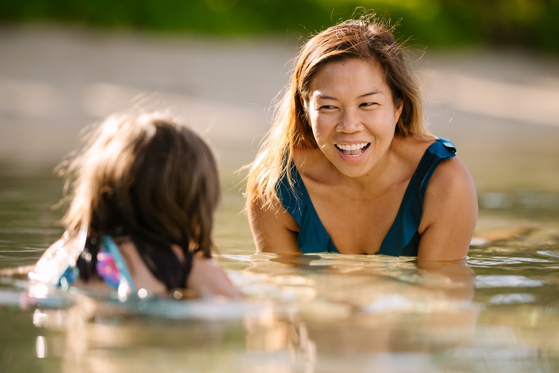 mom and daughter sharing a laugh in koolina lagoon during a family portrait session