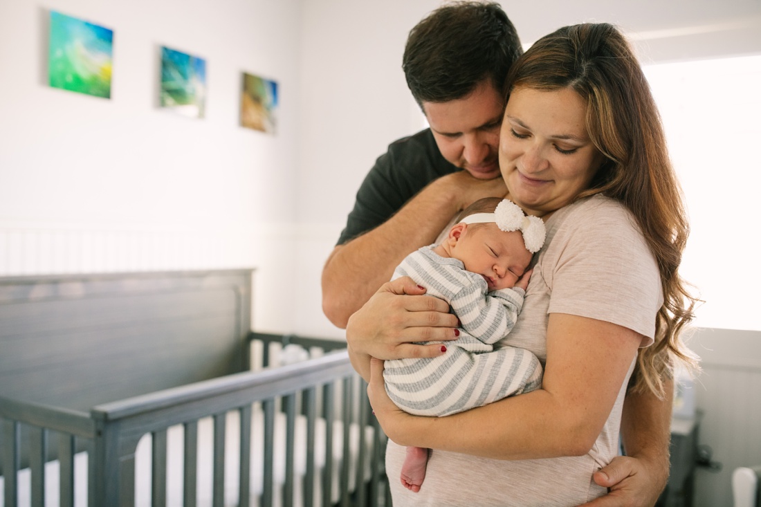 mom and dad cuddle newborn in the nursery during a newborn photography session in oahu