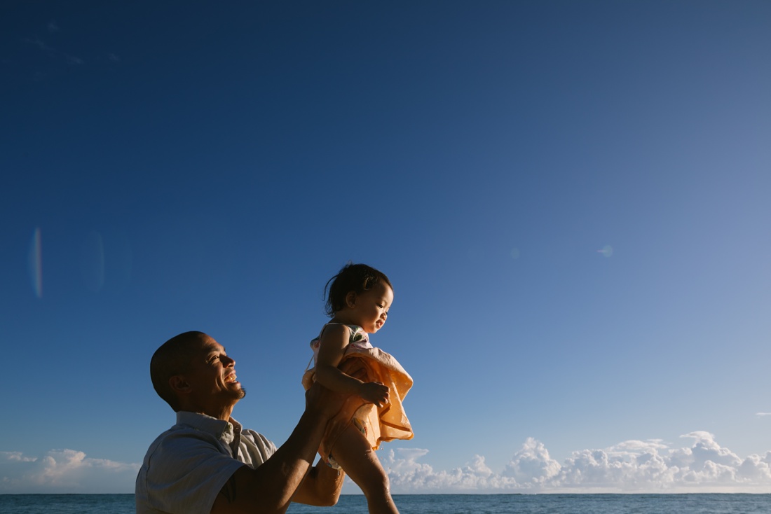dad holds daughter in the air at sunrise over lanikai beach during a family photogrpahy session in hawaii