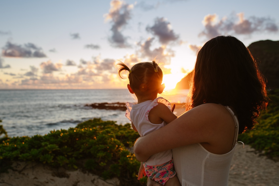 mom and toddler daughter watch sunrise in hawaii during a family photo session by little bird photography