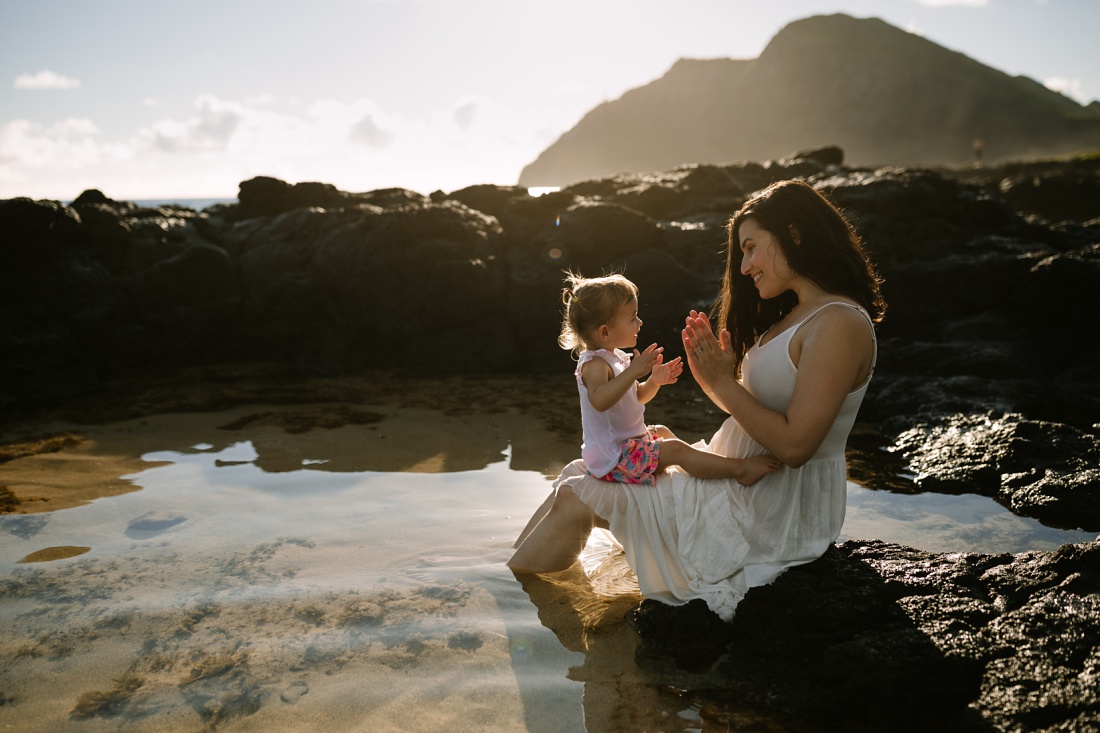 mom and daughter play pattycakes in the tidepools of makapuu beach in hawaii