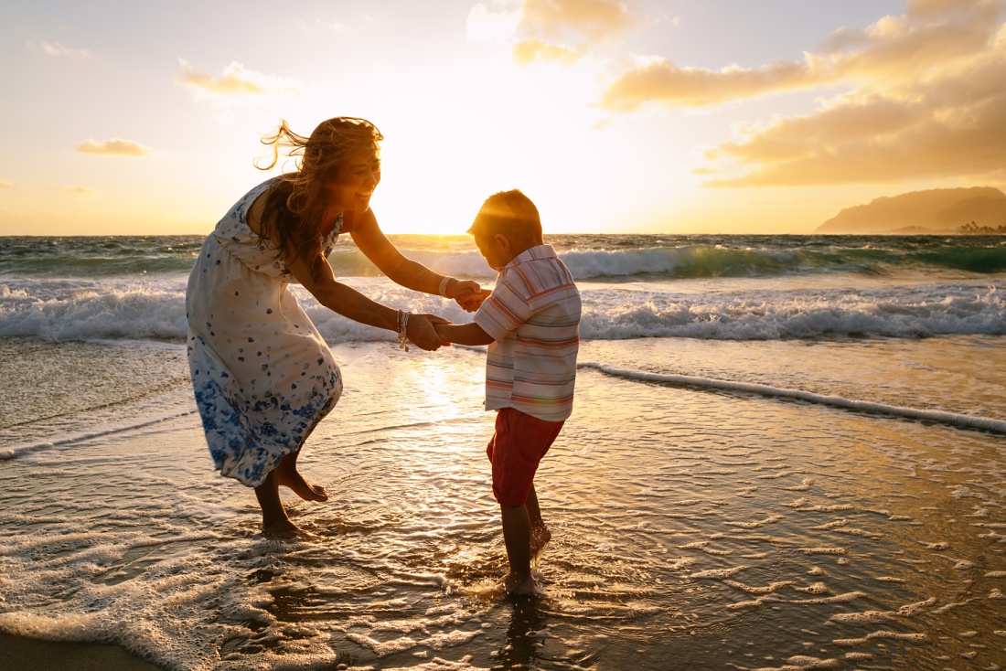 mom and son dance in the waves at sunrise in hawaii during a Fun Family Photography Session