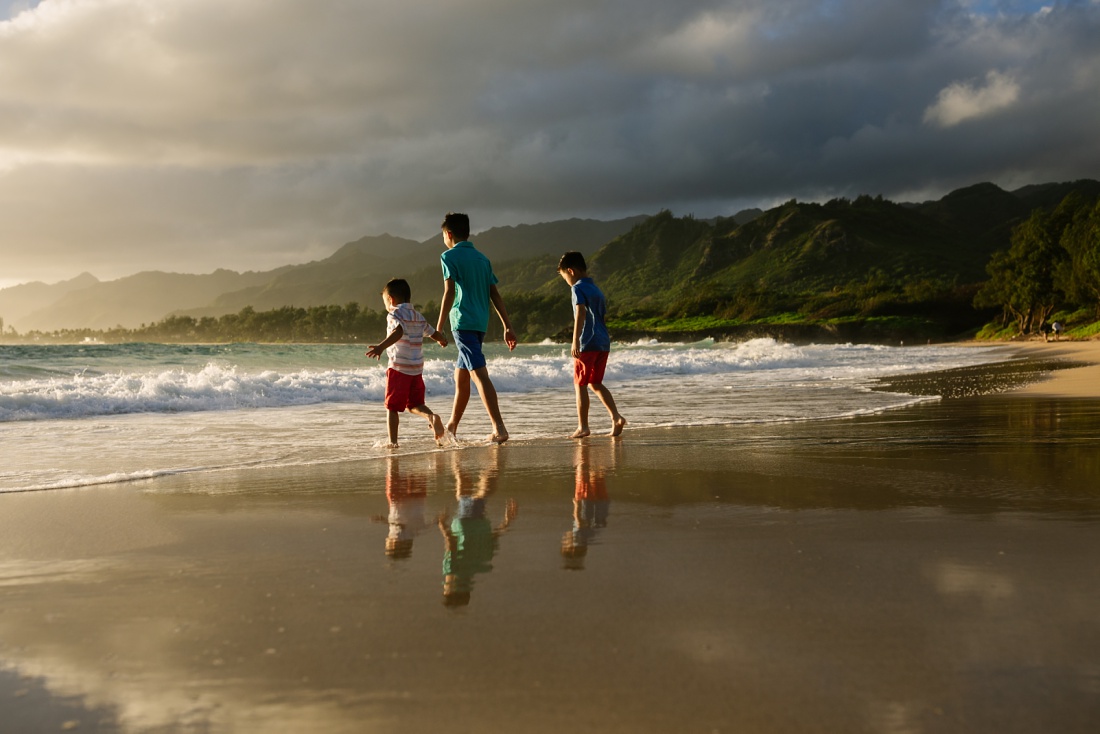 brothers walking on the beach with reflections of mountains behind at laie beach park