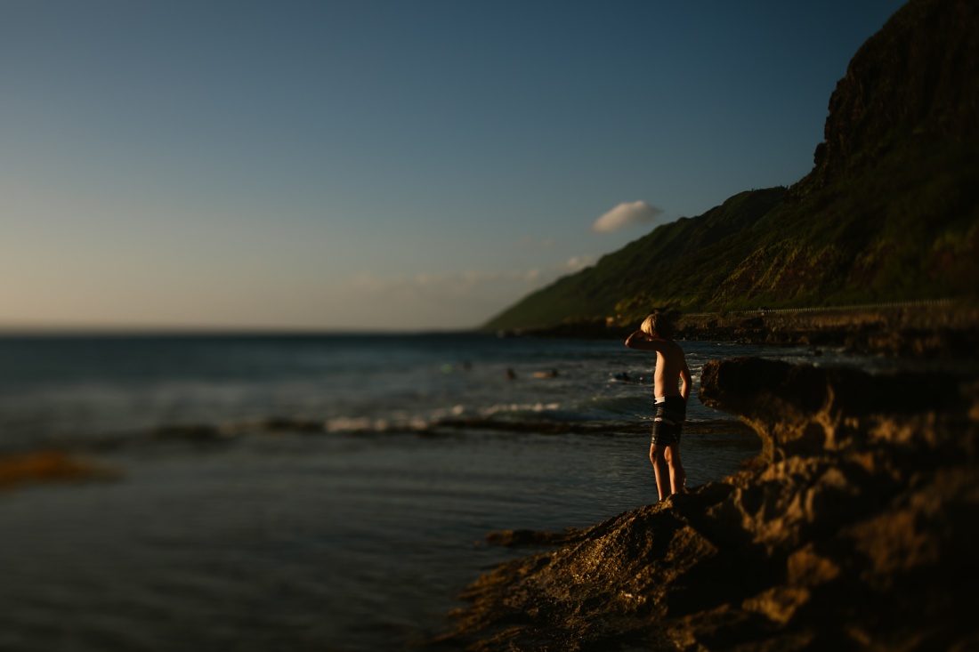 boy looking out at the surf at sunset on oahu