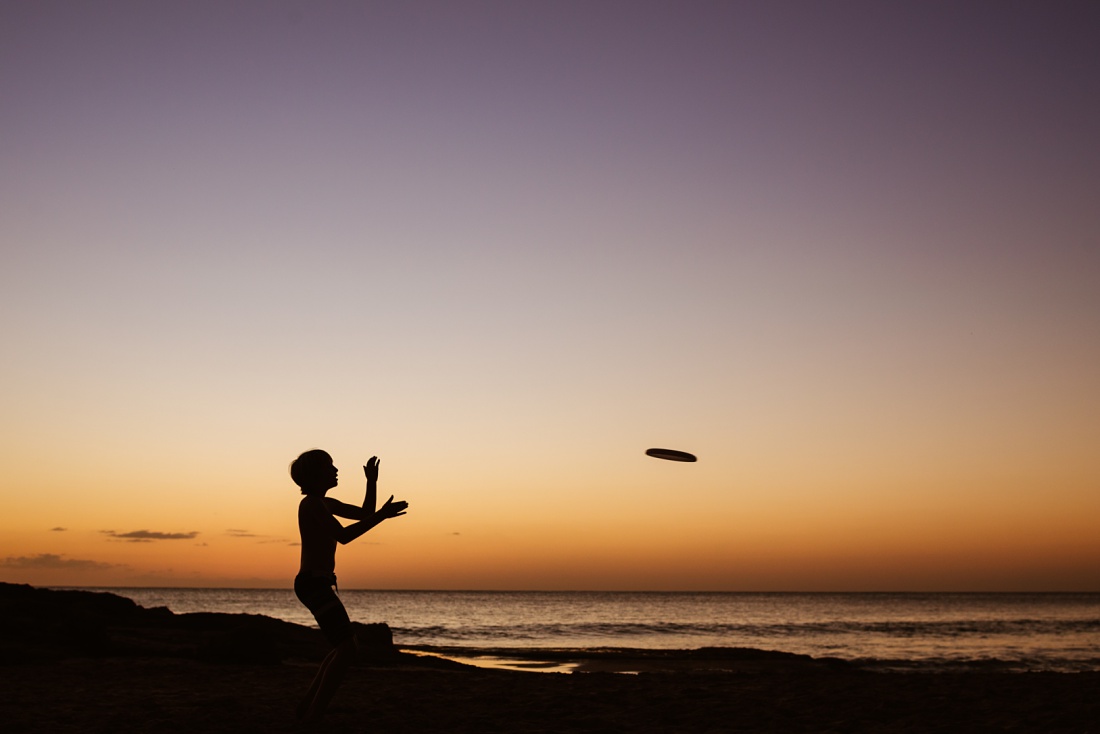 silhouette of a boy catching a Frisbee at sunset in hawaii