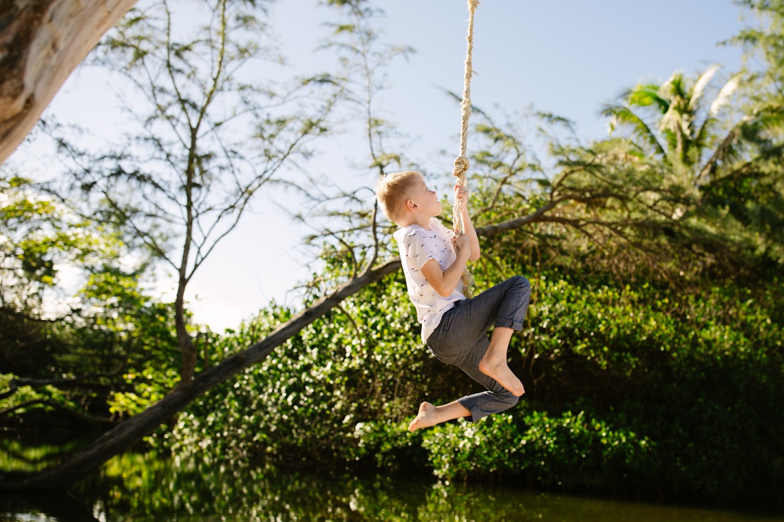 boy hangs from a rope swing at laie beach park