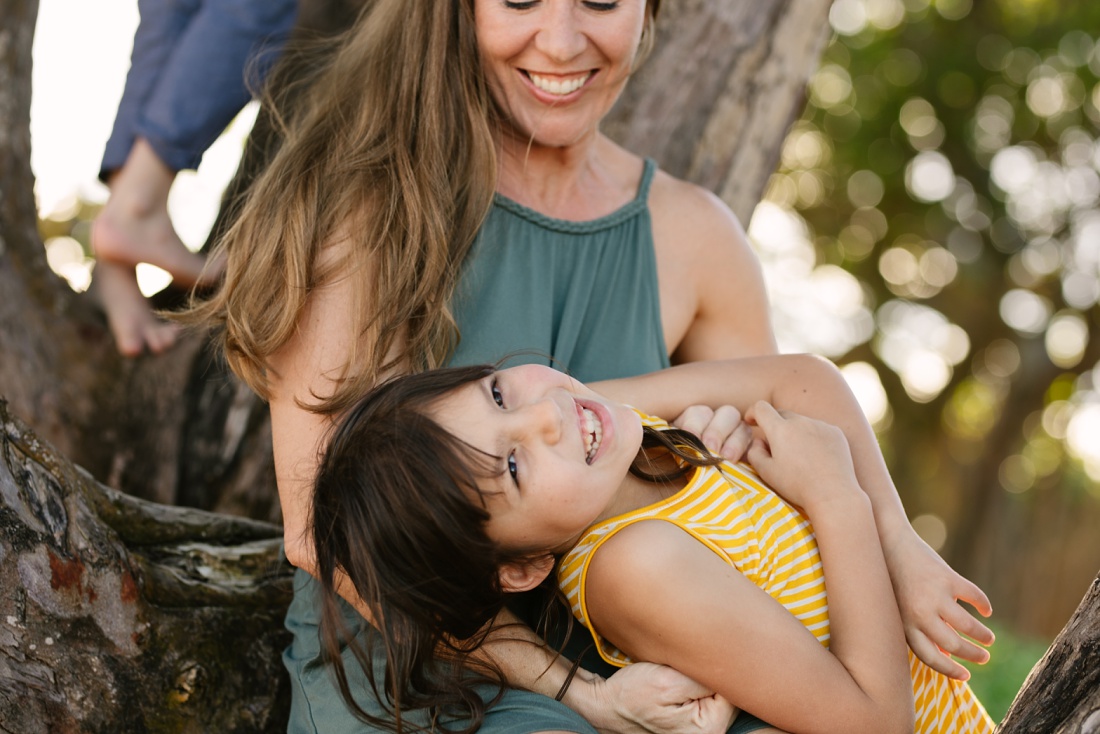 mom and daughter cuddle and laugh during a family portrait session at the beach in laie