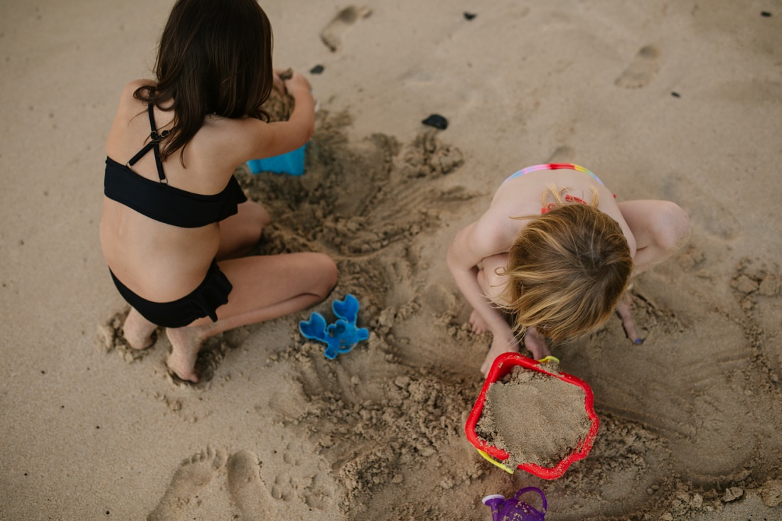 sisters build sand castles at the beach during a photo shoot in hawaii