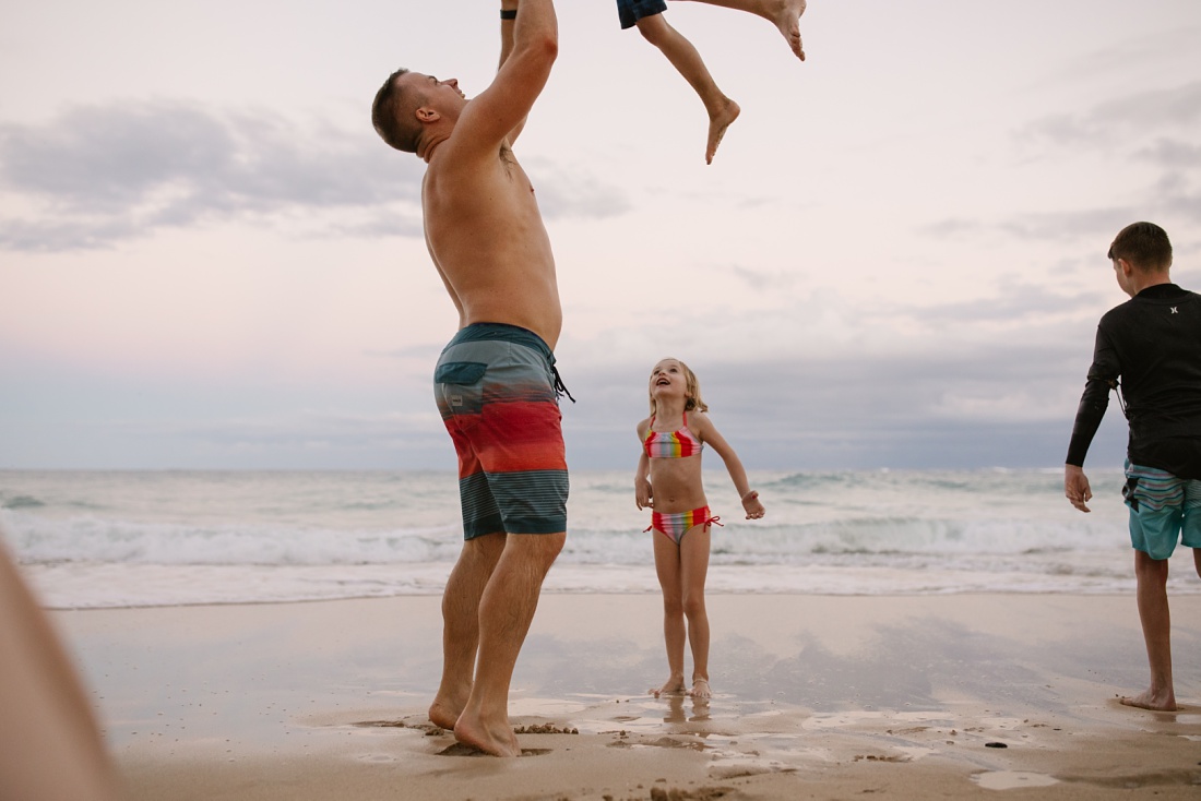 dad takes turns throwing his kids in the air during a family photoshoot in oahu