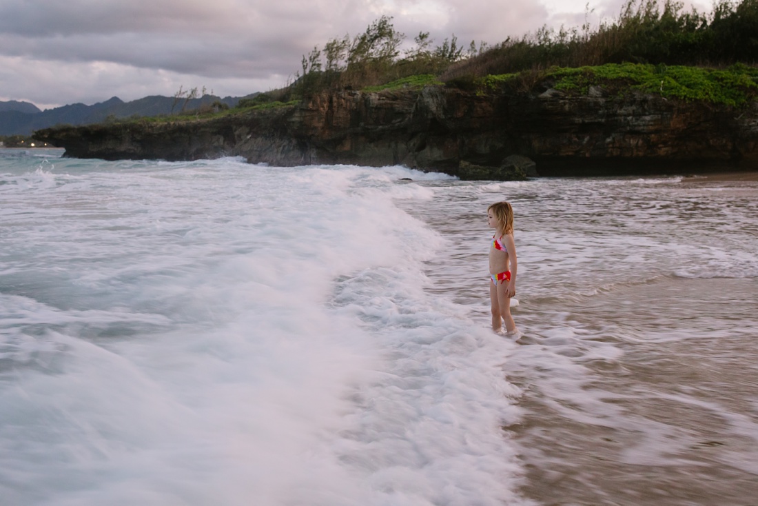 little girl standing in the rough waves at laie beach