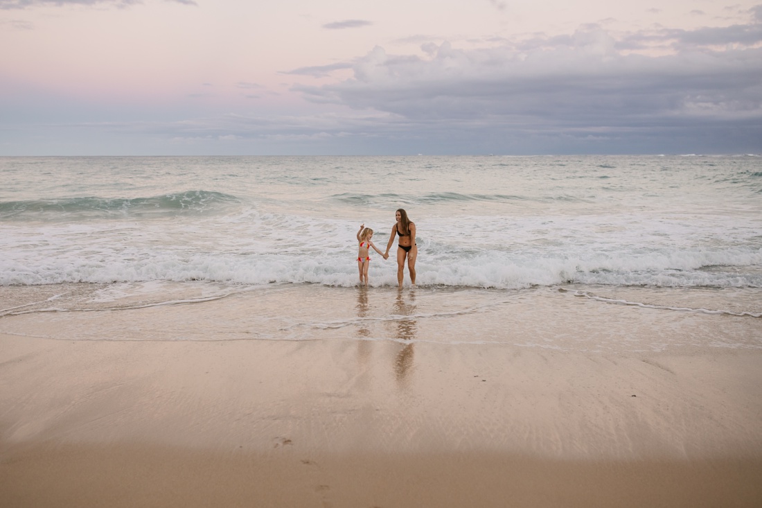 mom and daughter play in the surf in laie at sunset during a fun photo session