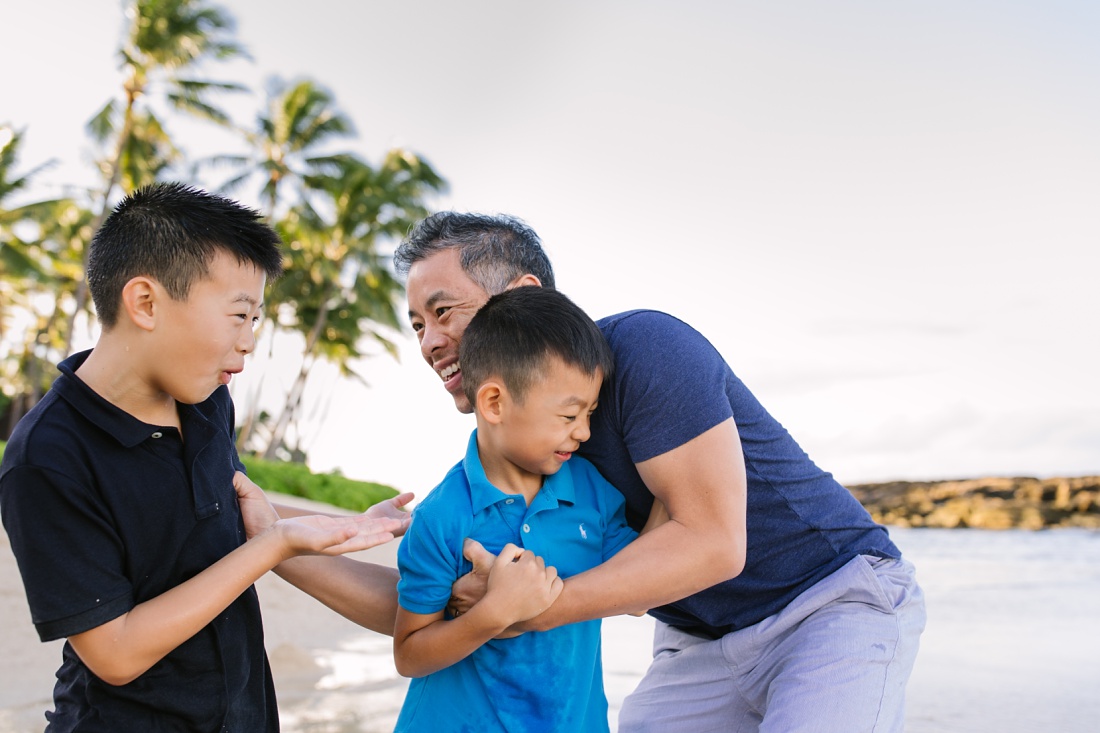 dad plays with sons at a beach in family-friendly beach in oahu
