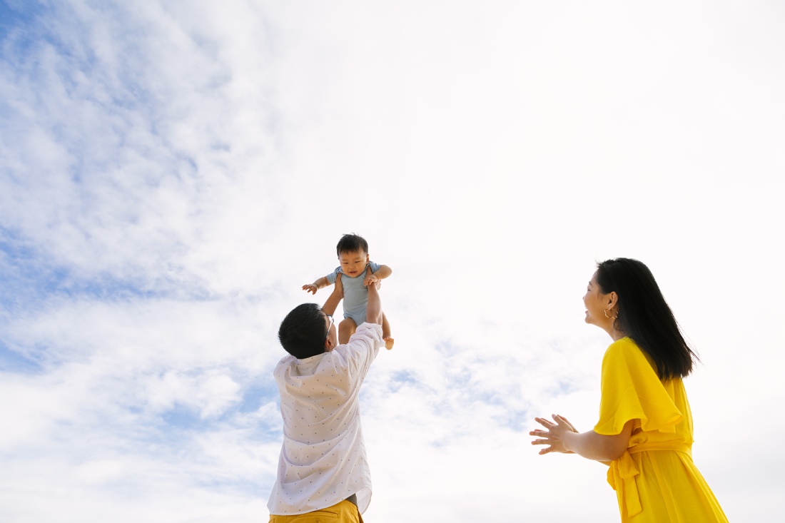 family holding baby in the air against a blue sky