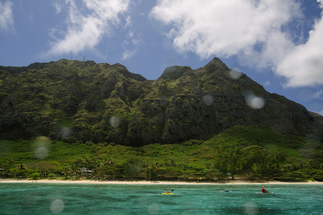 family of three paddles in waimanalo with the mountains behind