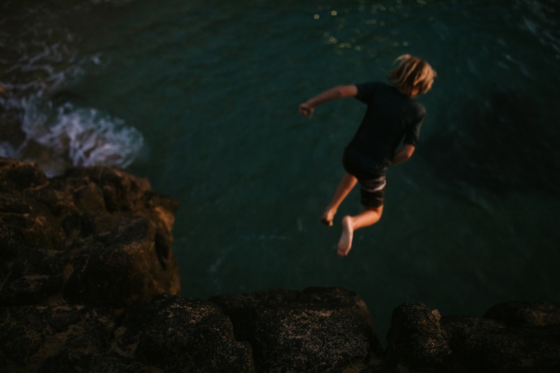 boy mid jump from the rock at waimea bay oahu