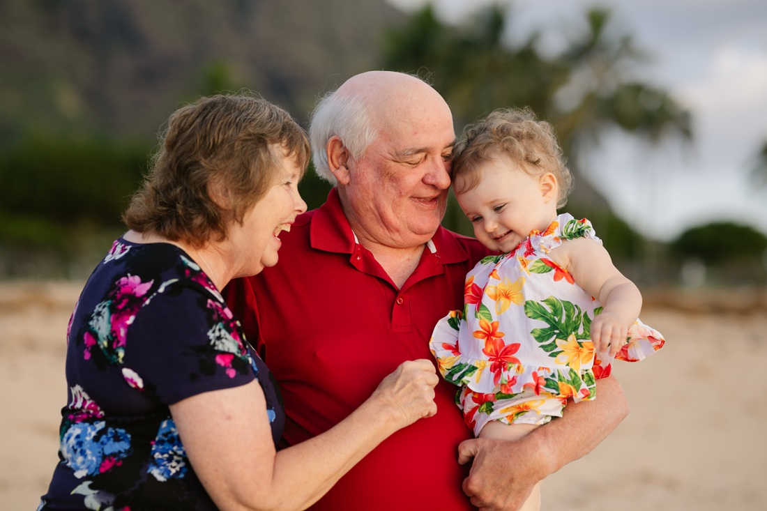 grandparents play with their grandchild during a family photo session at a beach in hawaii