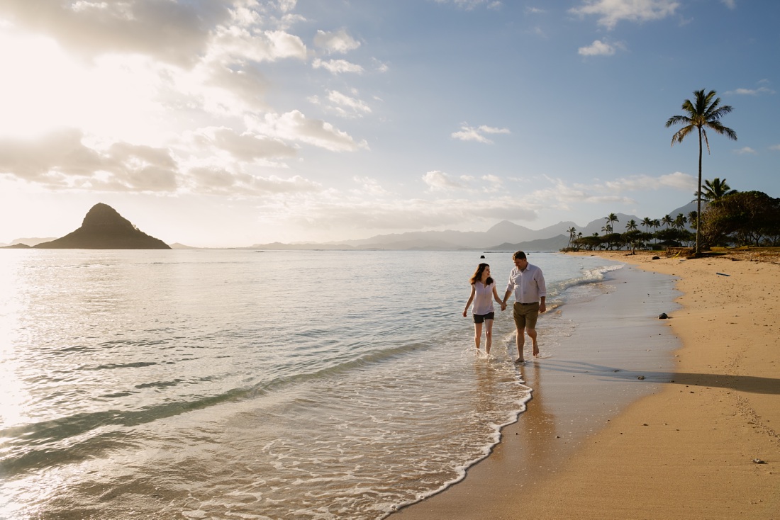 couple walking on the beach holding hands at kualoa beach park at sunrise