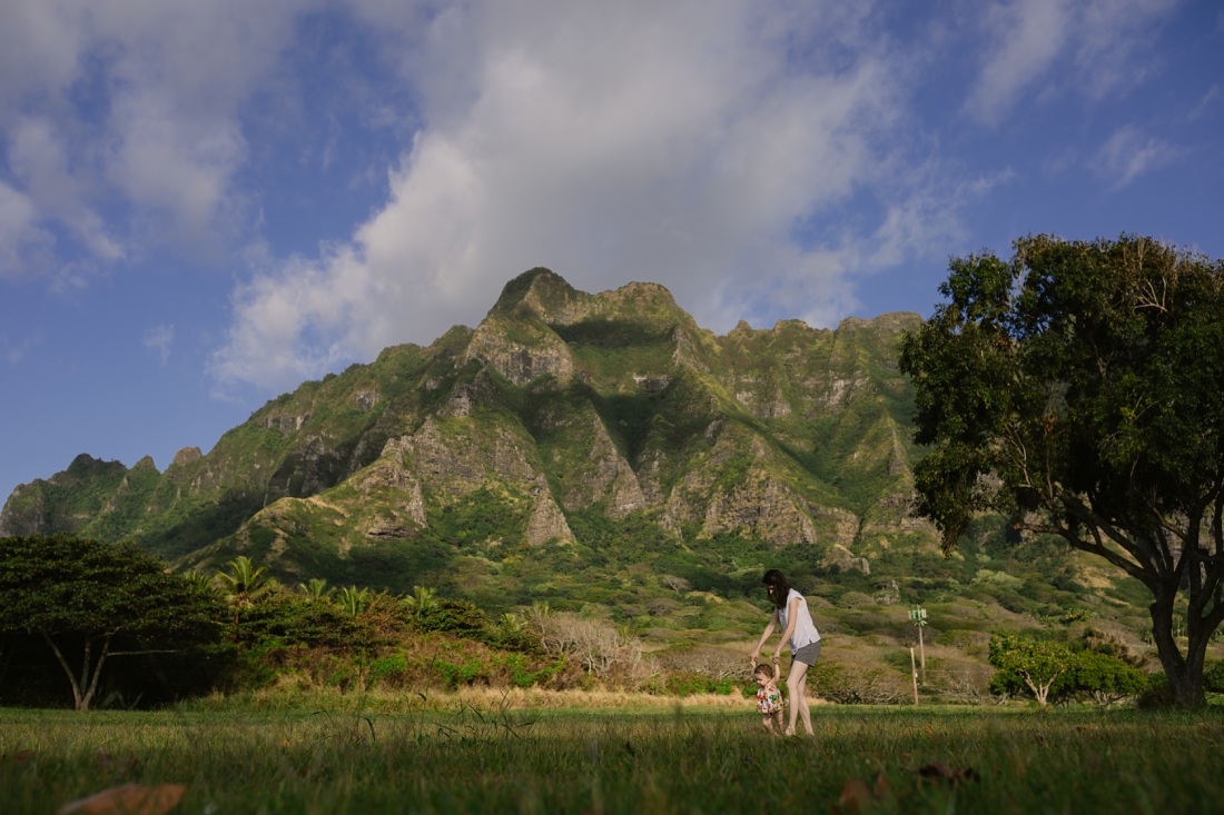 mom walks baby daughter with mountains behind at kualoa beach park oahu