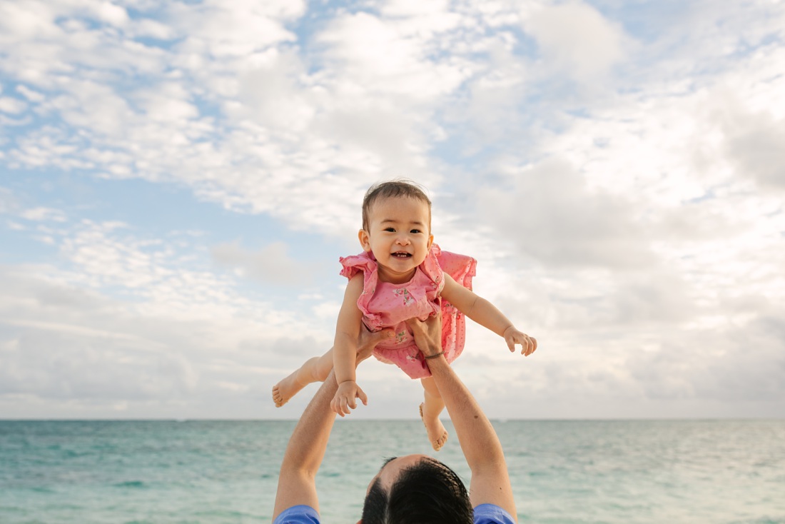 dad throws baby girl in the air at the beach in hawaii