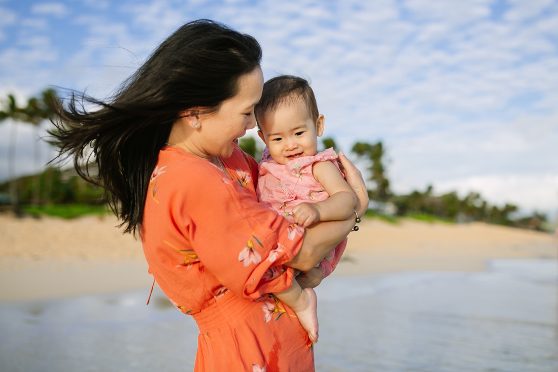 mom hugs baby girl at lanikai beach kailua during a family photography session