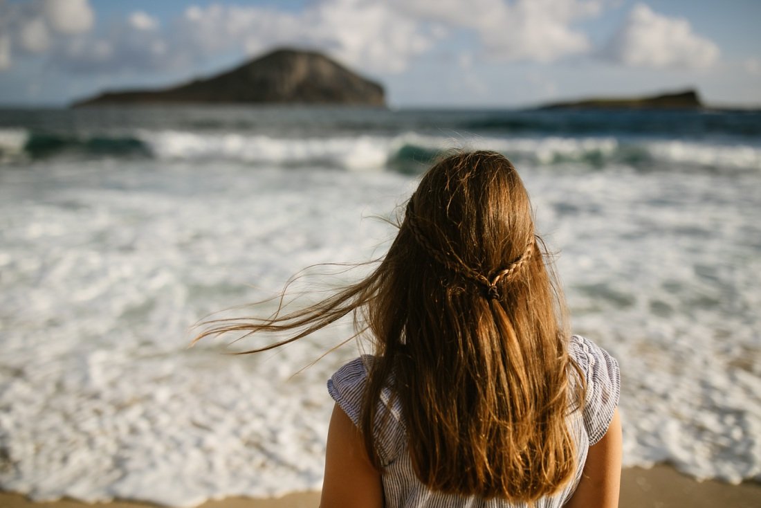girl watching the waves during a family portrait session in hawaii as the wind blows her hair