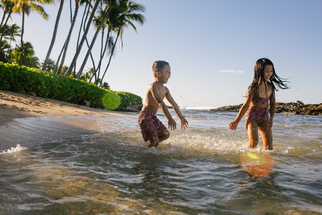 siblings splashing in the shallows at koolina lagoon during photo session at the beach