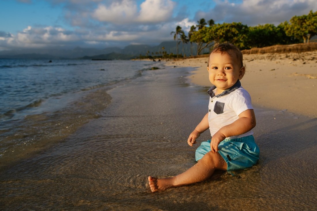 portrait of a baby sitting on the sand at sunrise for a photo session at kualoa beach oahu