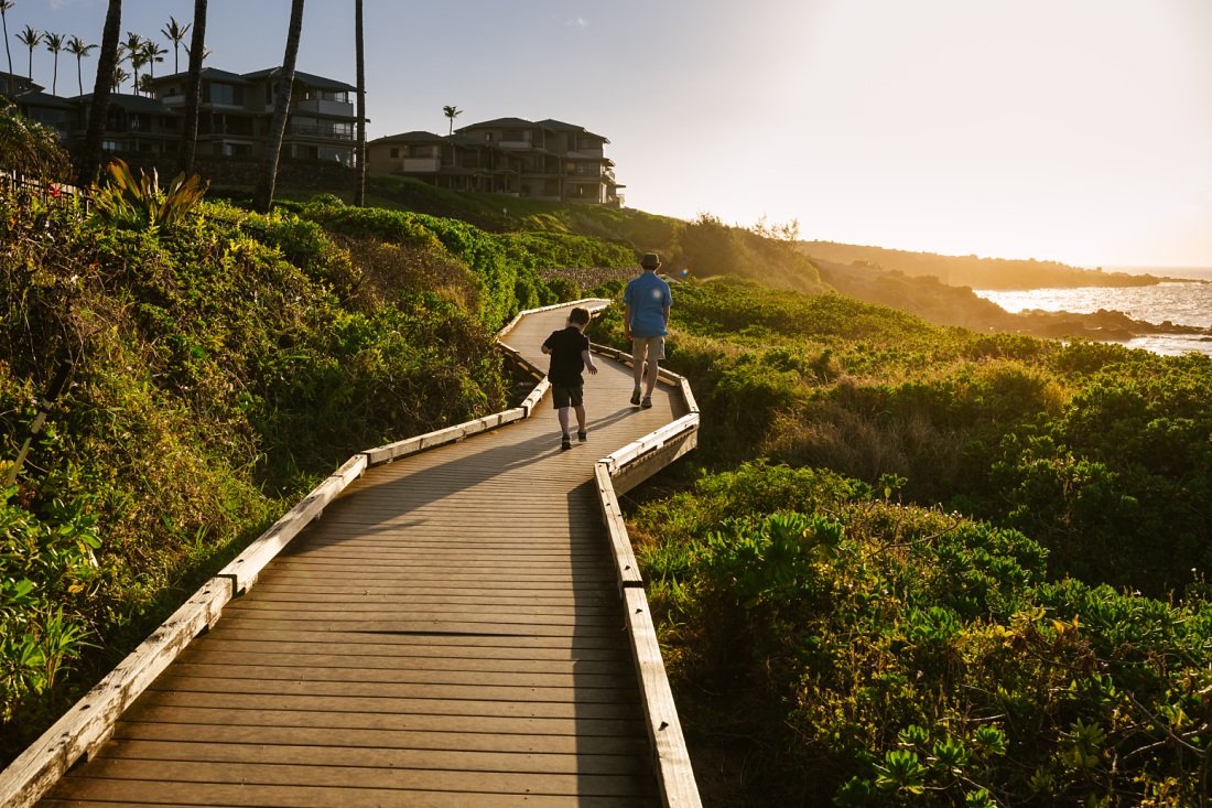 siblings running along the boardwalk at kapalua ironwoods beach at sunset