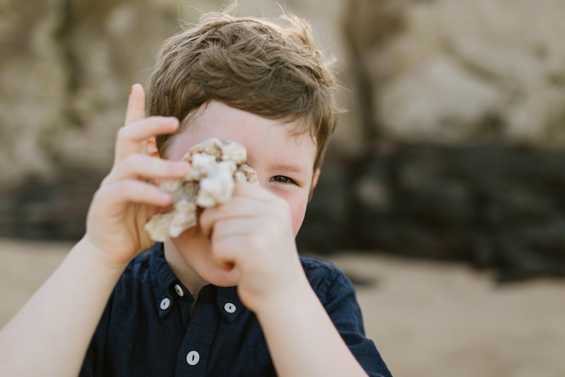boy pretending to take a photo with a piece of coral during a photo session in hawaii