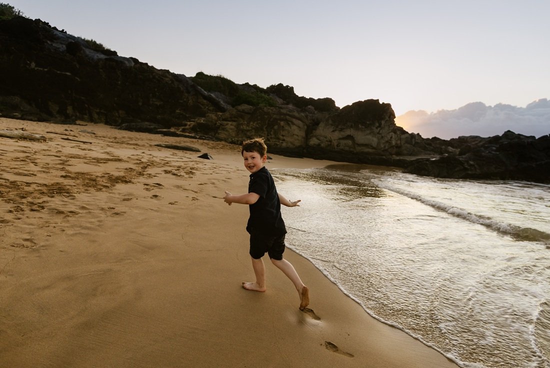 boy running along the shore with cliffs behind at sunset on maui