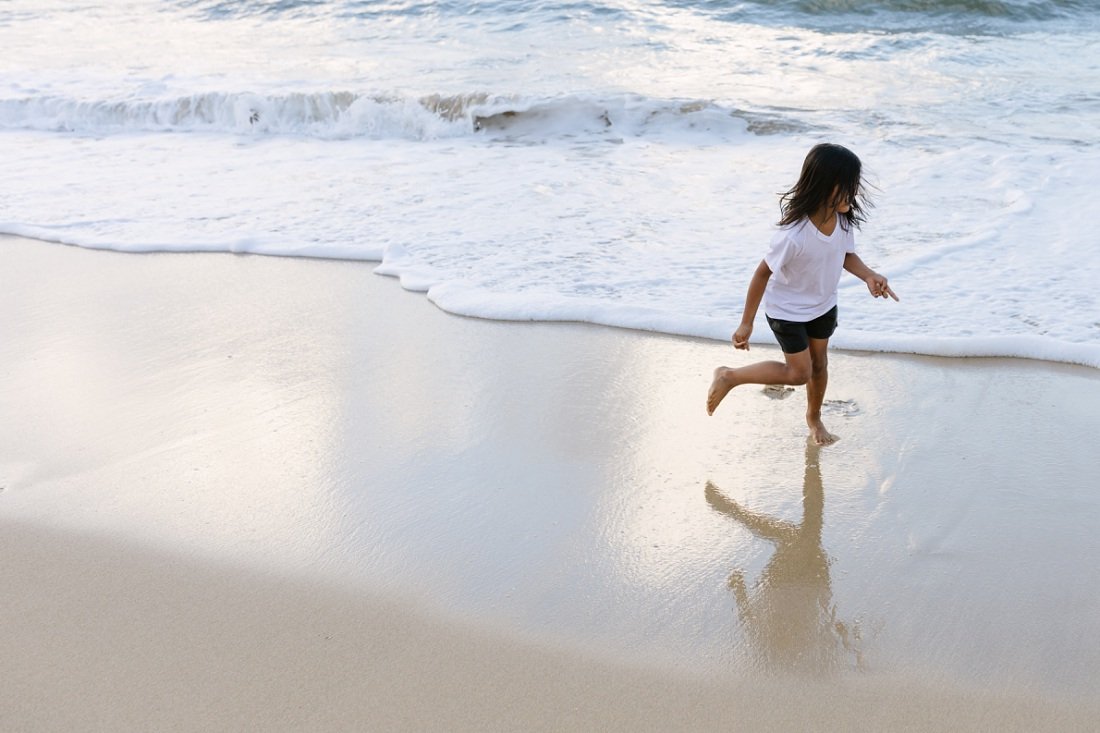 boy running along the beach with reflection in oahu