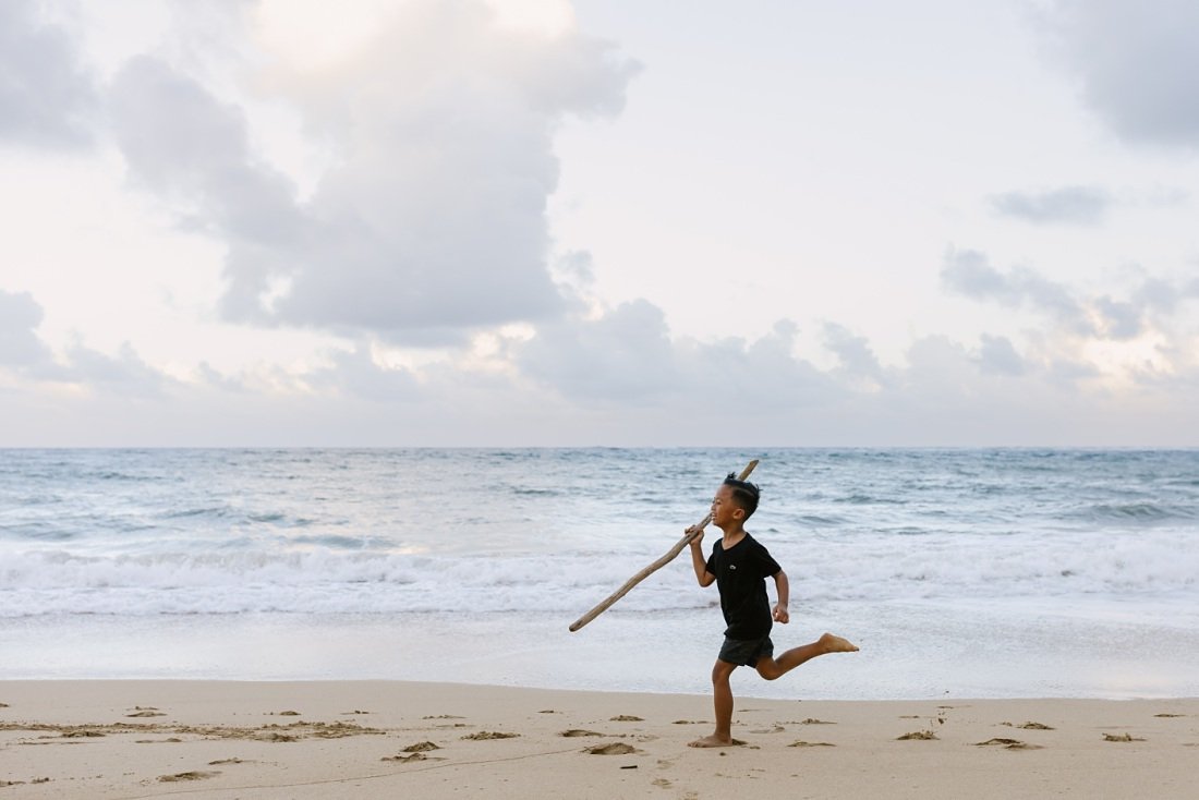 boy running along the beach with a stick in hawaii 
