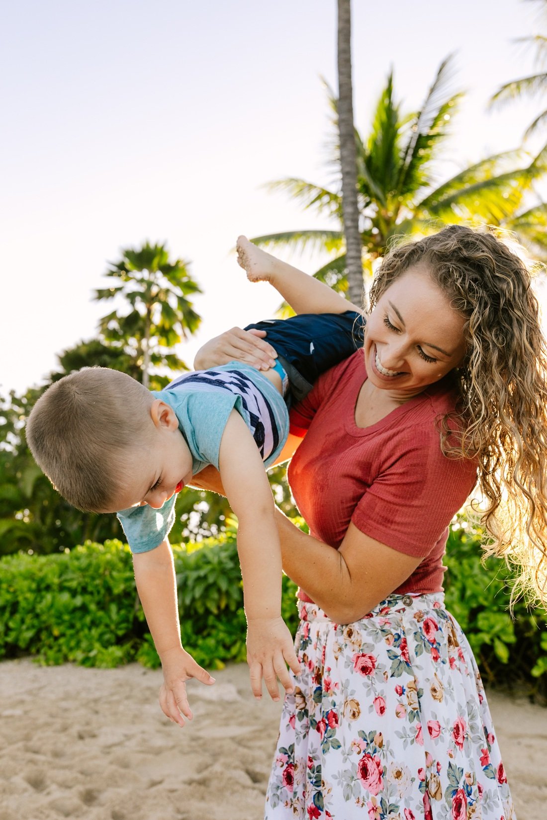 mom holds son upside-down while they laugh during koolina photo shoot