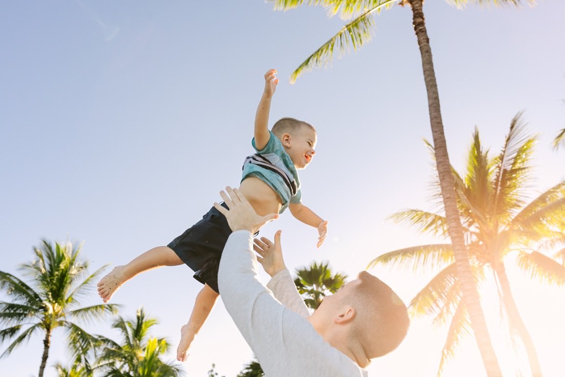 dad throws son in the air with sun and palm trees in hawaii