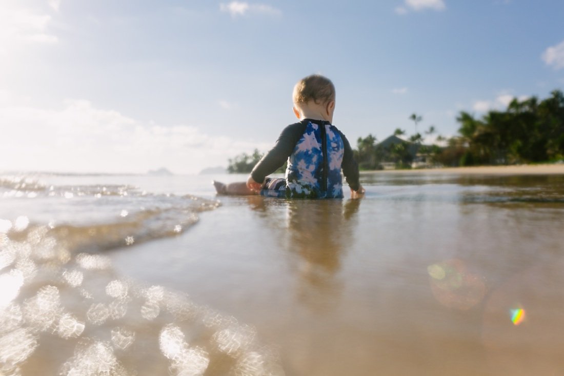 baby boy sits in the surf captured at a low angle by Family photographers in Oahu