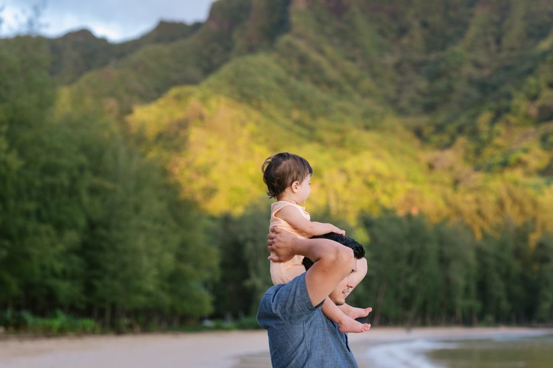 dad carrying baby on shoulders with mountains behind at kahana bay
