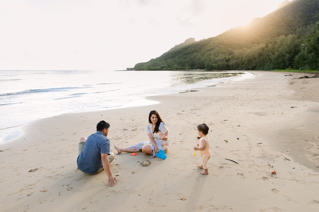 family with a baby plays on an empty beach in hawaii
