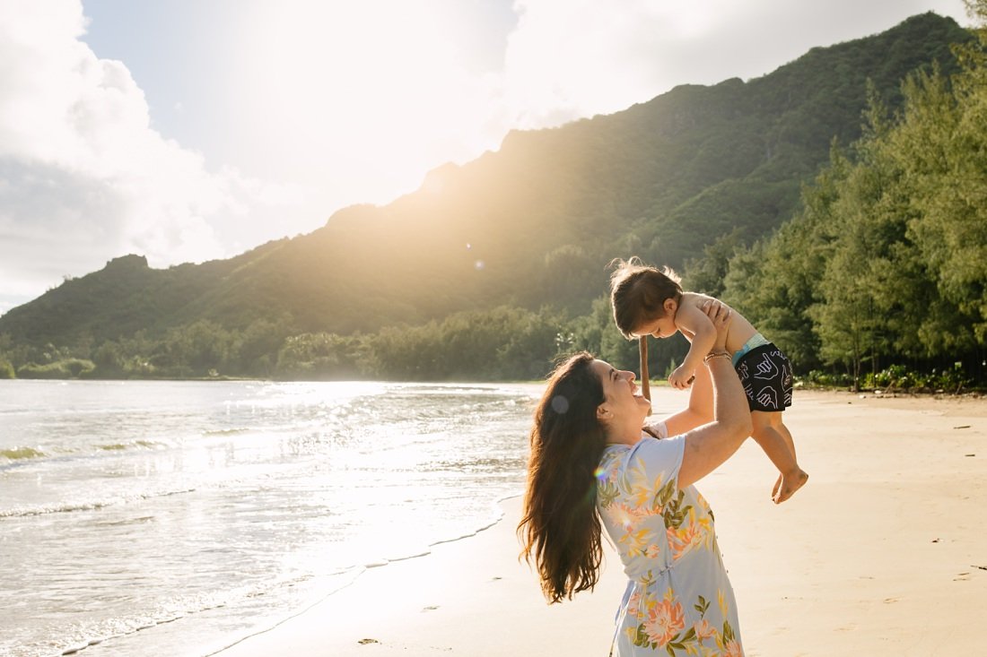 mom holding baby in the air at kahana bay at sunrise during Hawaii family beach portraits