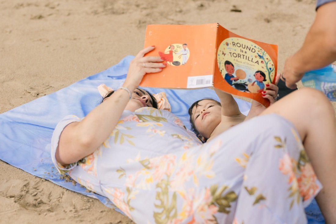 mom reading a book to baby son on the beach in oahu