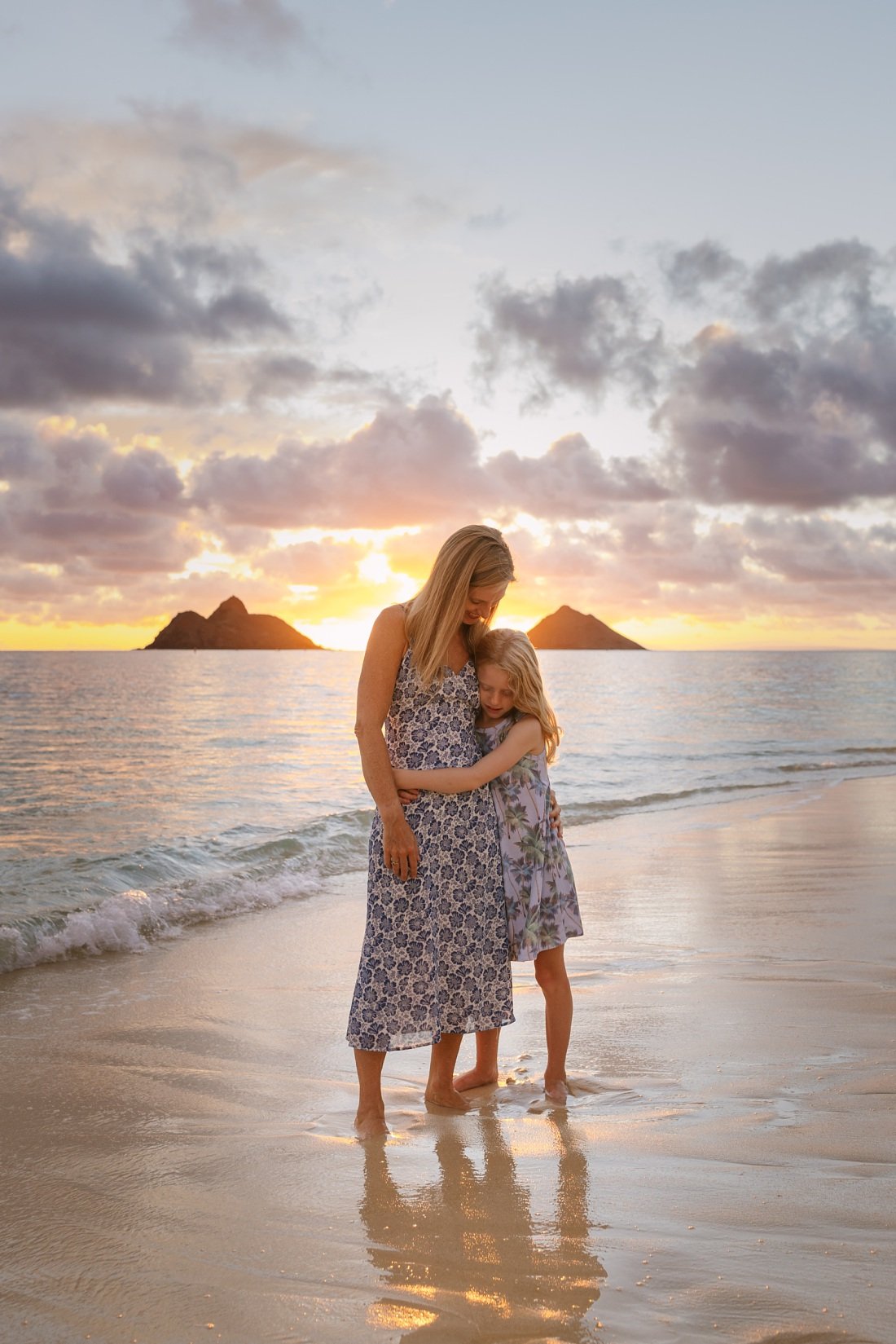 mom and daughter hug with the mokulua islets behind at sunrise