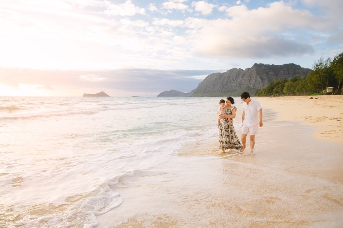 family with a baby walking on waimanalo beach at sunrise for a family photoshoot