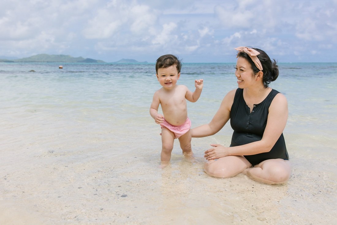 mom and baby play on a clear calm beach in hawaii