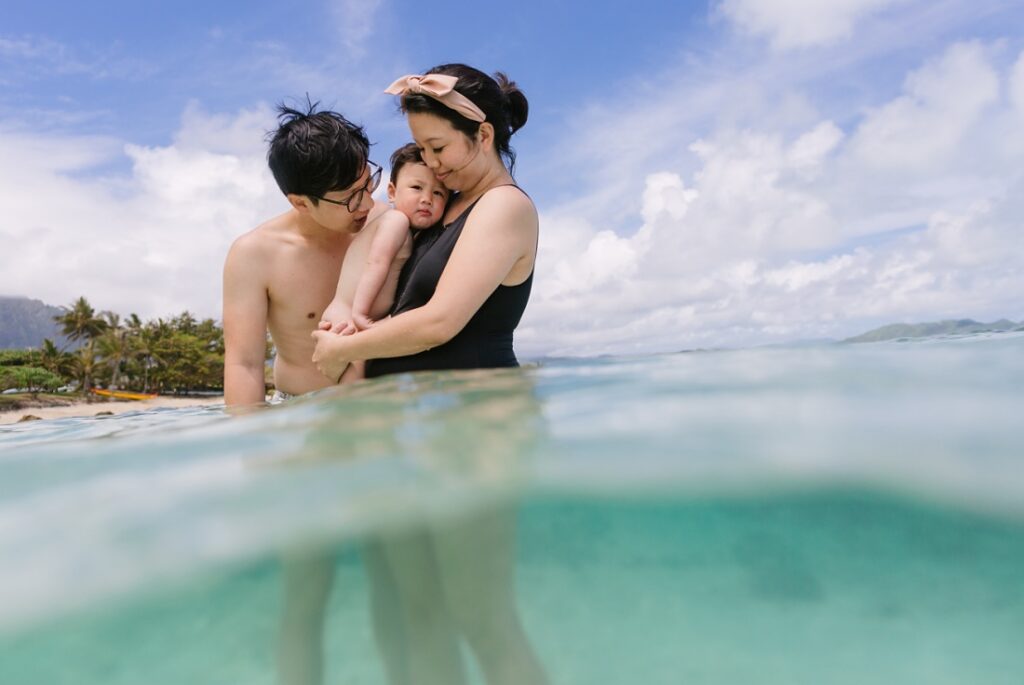 family snuggle in the clear blue water of kaiona beach oahu