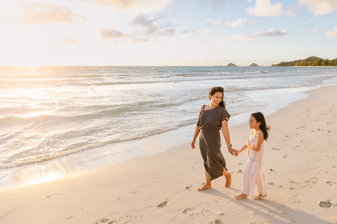 mom and daughter walk along kailua beach at sunrise