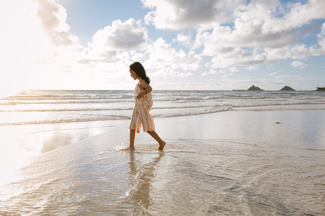 girl walking in the shallows of kailua beach with mokes in the background