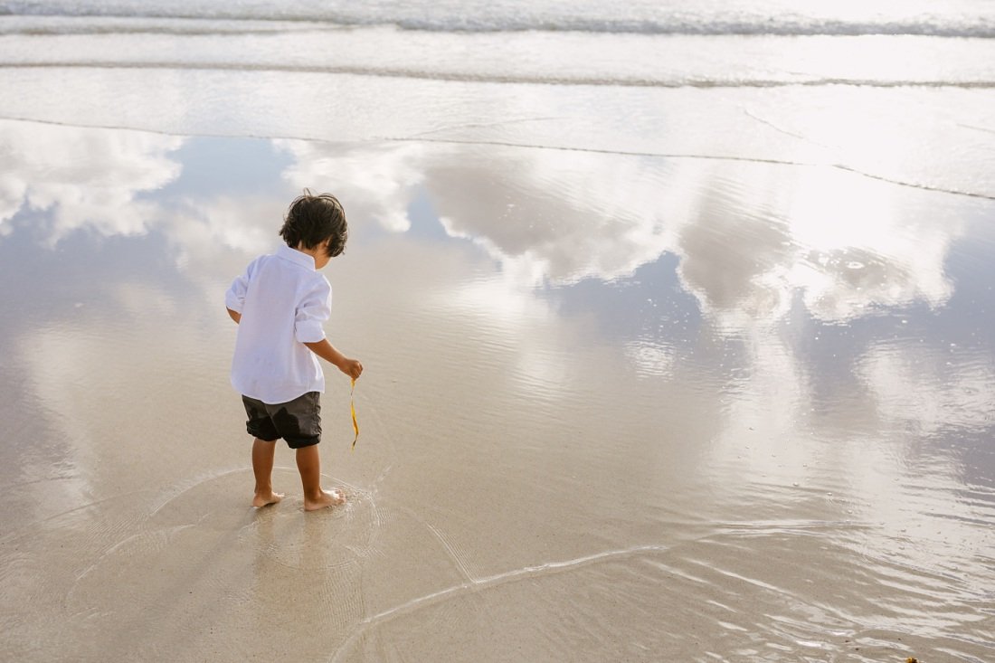 boy playing in the shallows at kailua beach with cloud reflections