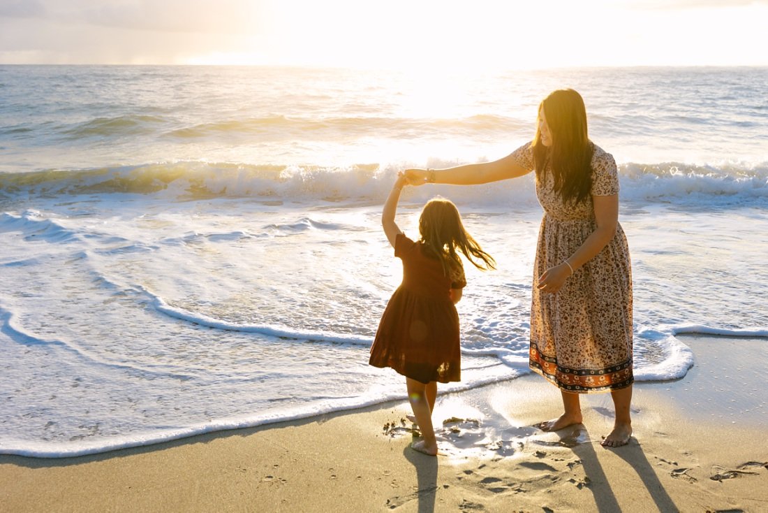 mom twirls daughter in golden sunlight at the beach in hawaii