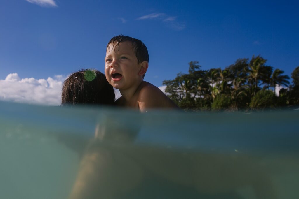 boy riding on moms back in the blue waters of laie oahu
